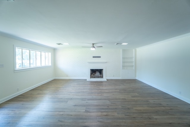 unfurnished living room with built in shelves, ceiling fan, a brick fireplace, dark hardwood / wood-style floors, and ornamental molding