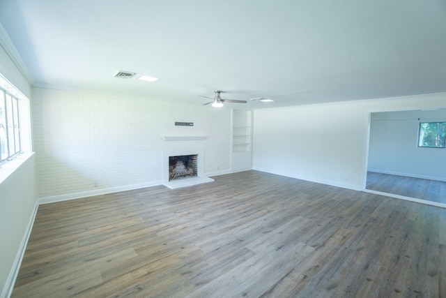 unfurnished living room featuring built in shelves, ceiling fan, a brick fireplace, brick wall, and wood-type flooring