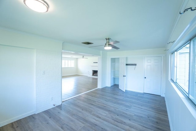 unfurnished room featuring ceiling fan, a large fireplace, dark wood-type flooring, and ornamental molding