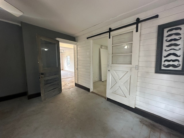 hallway featuring a barn door, concrete flooring, and wooden walls