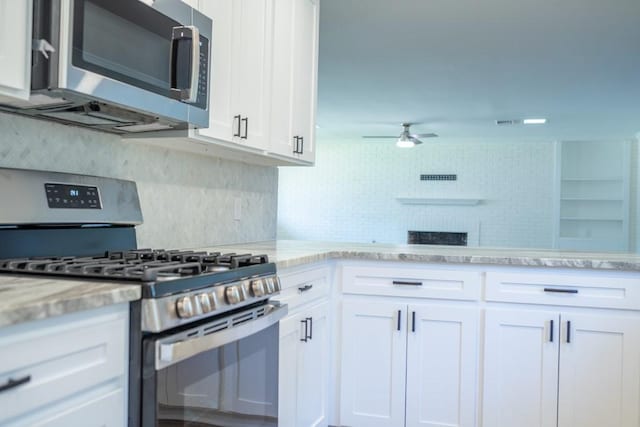 kitchen with ceiling fan, decorative backsplash, a fireplace, white cabinets, and appliances with stainless steel finishes