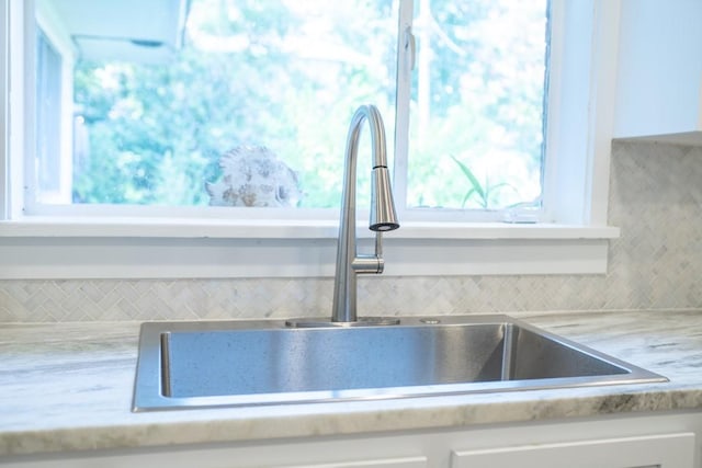 room details with tasteful backsplash, white cabinetry, and sink