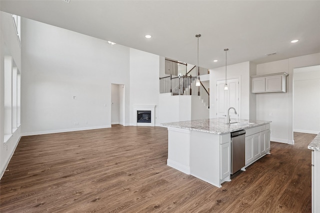 kitchen featuring hanging light fixtures, sink, white cabinetry, light stone countertops, and a kitchen island with sink