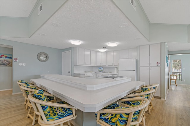 kitchen with white fridge, light wood-type flooring, white cabinetry, and a textured ceiling