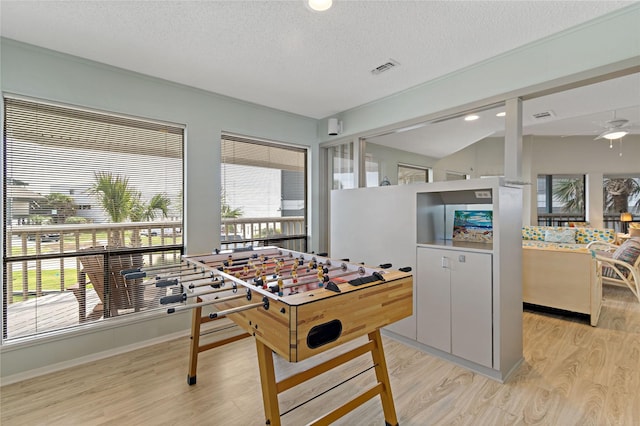 recreation room featuring vaulted ceiling, ceiling fan, light hardwood / wood-style flooring, and a textured ceiling