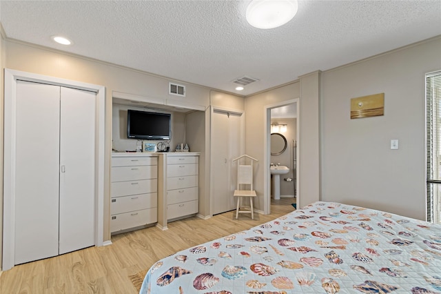bedroom with multiple closets, ensuite bathroom, a textured ceiling, and light wood-type flooring