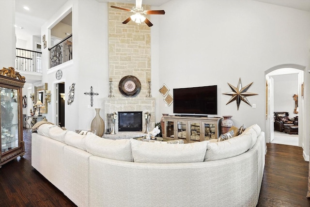 living room with dark hardwood / wood-style floors, a high ceiling, a stone fireplace, and ceiling fan