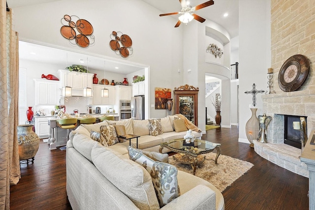 living room featuring dark hardwood / wood-style floors, a fireplace, a high ceiling, and ceiling fan