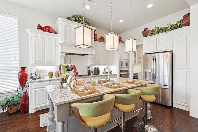 kitchen featuring decorative light fixtures, white cabinets, appliances with stainless steel finishes, and a kitchen island with sink