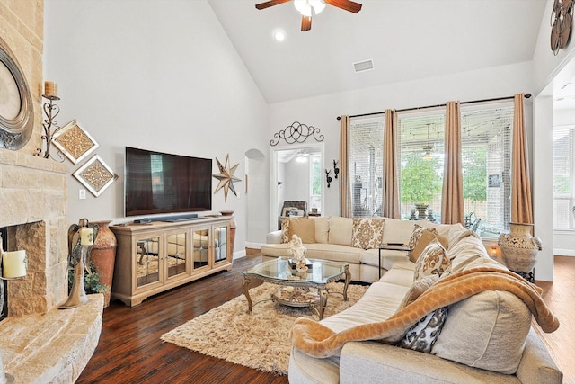 living room with ceiling fan, dark wood-type flooring, high vaulted ceiling, and a stone fireplace