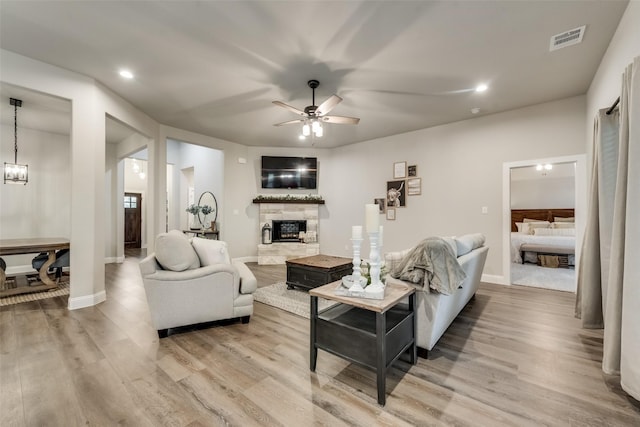 living room featuring light hardwood / wood-style floors, a stone fireplace, and ceiling fan with notable chandelier