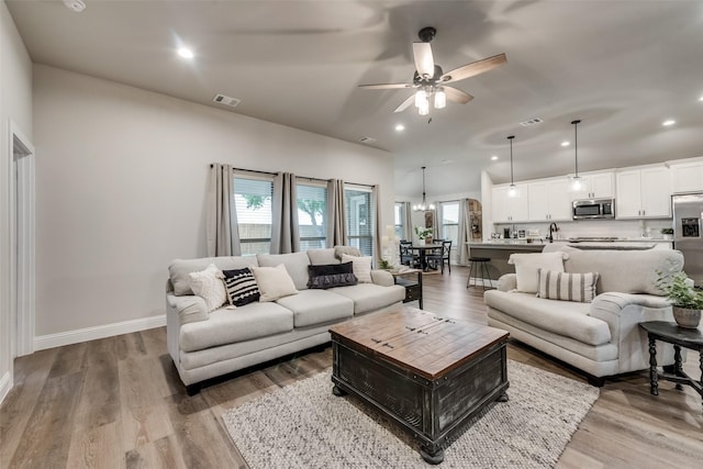 living room with ceiling fan with notable chandelier and light wood-type flooring