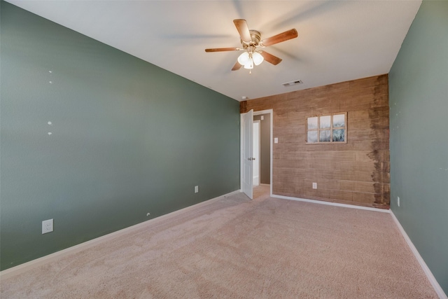 carpeted empty room with ceiling fan and wooden walls