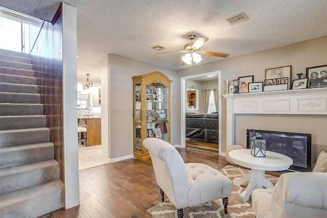 living room featuring ceiling fan with notable chandelier, a textured ceiling, and hardwood / wood-style flooring