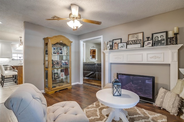 living room with a textured ceiling, ceiling fan, and wood-type flooring