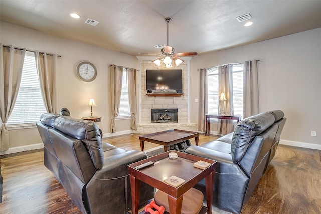 living room with a stone fireplace, ceiling fan, wood-type flooring, and a wealth of natural light