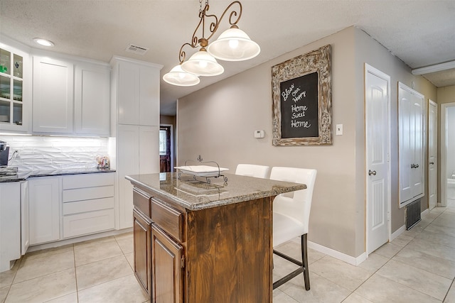 kitchen with hanging light fixtures, light tile patterned floors, dark stone countertops, a center island, and white cabinetry