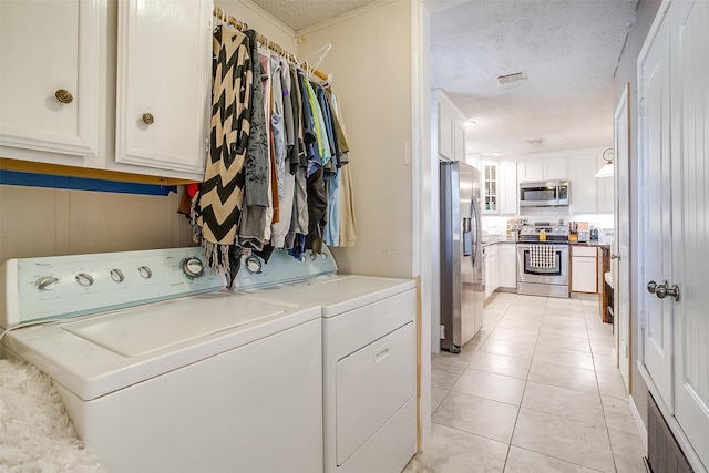 clothes washing area with cabinets, washer and dryer, a textured ceiling, and light tile patterned floors