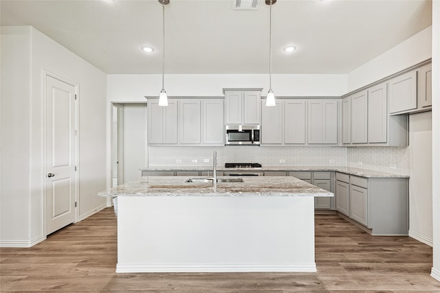 kitchen featuring light stone countertops, a kitchen island with sink, wood-type flooring, and hanging light fixtures