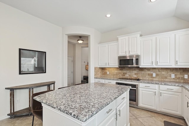 kitchen featuring backsplash, appliances with stainless steel finishes, light stone counters, white cabinetry, and a kitchen island