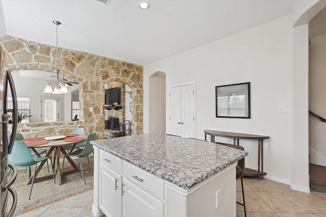 kitchen with a kitchen island, light stone countertops, hanging light fixtures, a breakfast bar area, and white cabinets