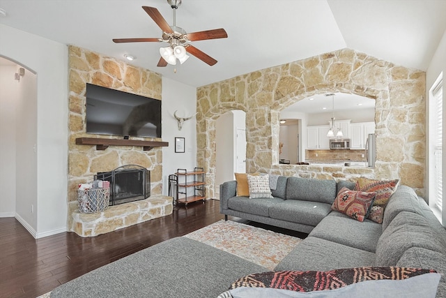 living room with ceiling fan with notable chandelier, dark hardwood / wood-style flooring, a stone fireplace, and lofted ceiling