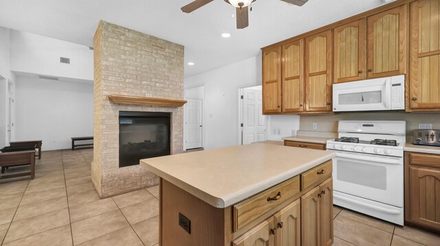 kitchen with a center island, white appliances, a brick fireplace, ceiling fan, and light tile patterned floors