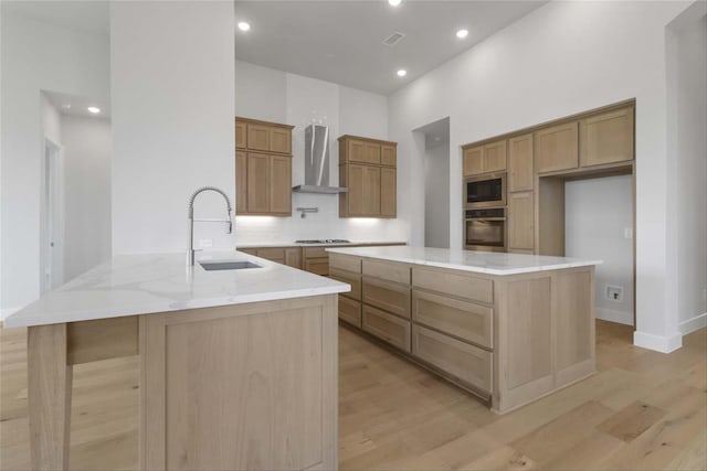 kitchen with stainless steel appliances, sink, kitchen peninsula, light wood-type flooring, and wall chimney exhaust hood