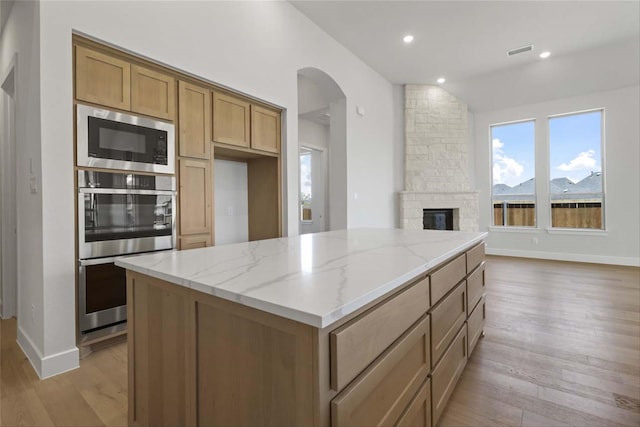 kitchen with light hardwood / wood-style flooring, a center island, stainless steel appliances, light stone countertops, and a stone fireplace