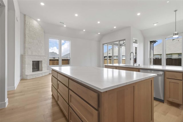 kitchen with a stone fireplace, sink, light wood-type flooring, a center island, and dishwasher