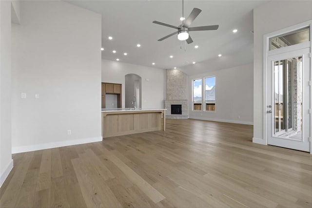 unfurnished living room featuring ceiling fan, high vaulted ceiling, light wood-type flooring, sink, and a stone fireplace