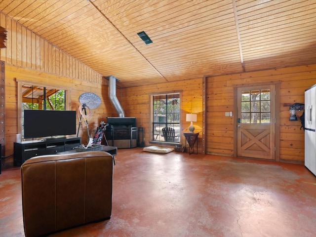 unfurnished living room featuring concrete flooring, wooden ceiling, a wood stove, lofted ceiling, and wood walls