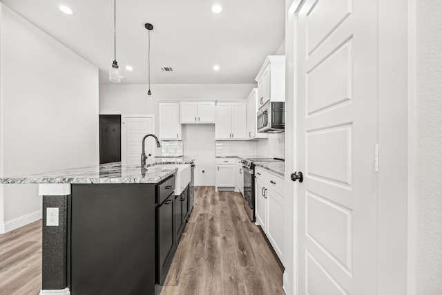 kitchen with white cabinetry, appliances with stainless steel finishes, light stone countertops, an island with sink, and light hardwood / wood-style floors