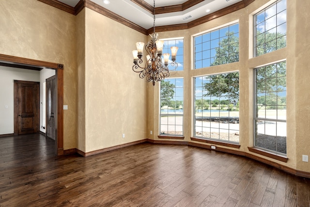 spare room featuring an inviting chandelier, a raised ceiling, dark hardwood / wood-style floors, a towering ceiling, and ornamental molding