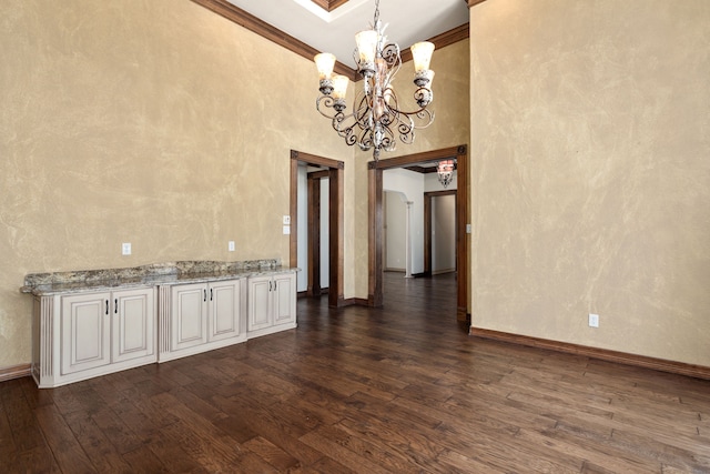 unfurnished dining area featuring dark hardwood / wood-style flooring, a chandelier, a high ceiling, and ornamental molding