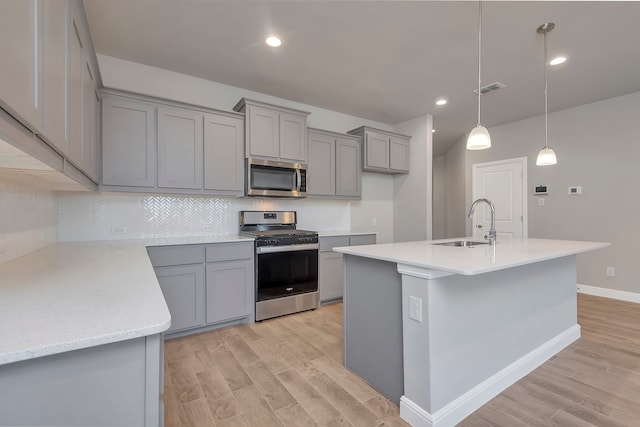 kitchen with stainless steel appliances, decorative backsplash, sink, a center island with sink, and light hardwood / wood-style flooring