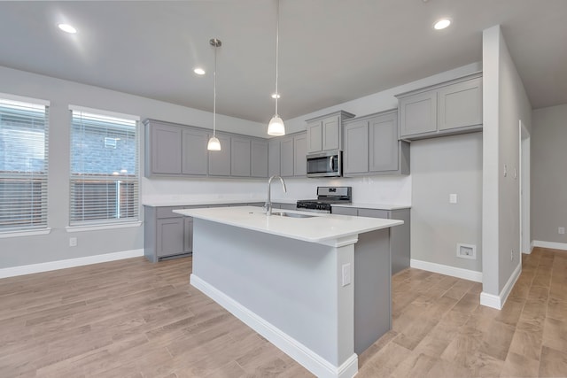 kitchen featuring pendant lighting, sink, light hardwood / wood-style floors, appliances with stainless steel finishes, and a kitchen island with sink