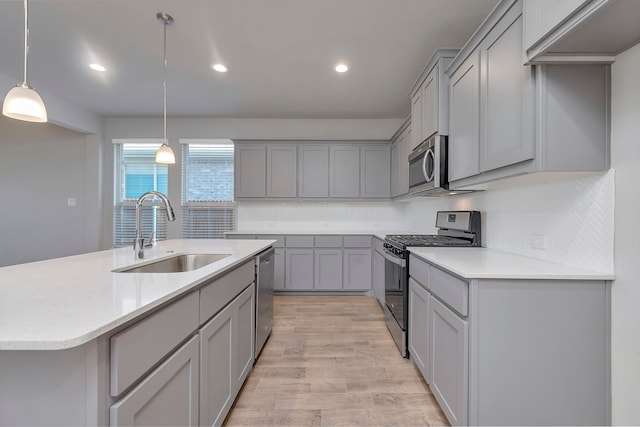 kitchen featuring stainless steel appliances, a center island with sink, sink, light hardwood / wood-style floors, and gray cabinets