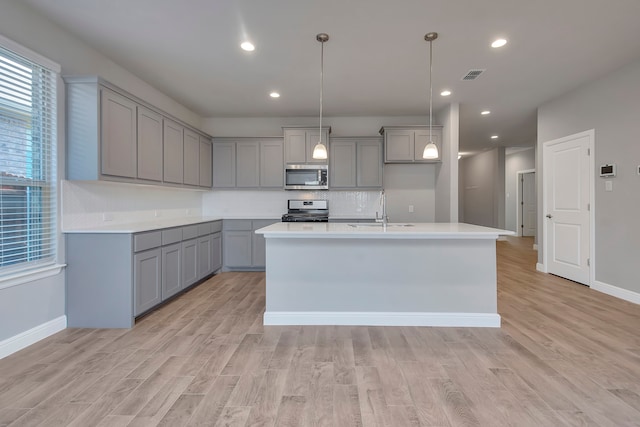 kitchen featuring light hardwood / wood-style flooring, backsplash, sink, stove, and a center island with sink