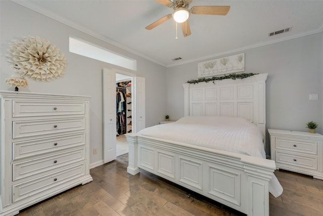 bedroom with crown molding, a spacious closet, dark hardwood / wood-style floors, a closet, and ceiling fan