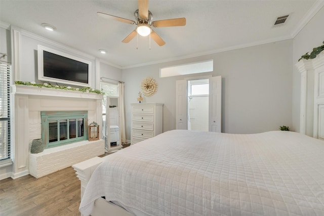 bedroom featuring ceiling fan, light hardwood / wood-style floors, crown molding, a brick fireplace, and a textured ceiling