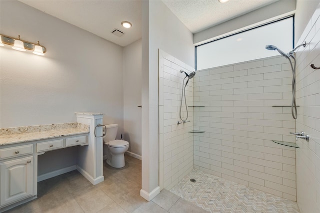 bathroom featuring tiled shower, toilet, a textured ceiling, vanity, and tile patterned flooring