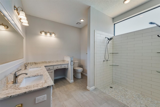 bathroom with vanity, tiled shower, a textured ceiling, and toilet