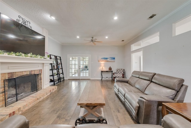 living room with crown molding, hardwood / wood-style flooring, ceiling fan, a fireplace, and a textured ceiling