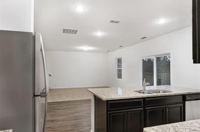 kitchen with a kitchen island with sink, stainless steel appliances, light stone counters, dark hardwood / wood-style floors, and sink