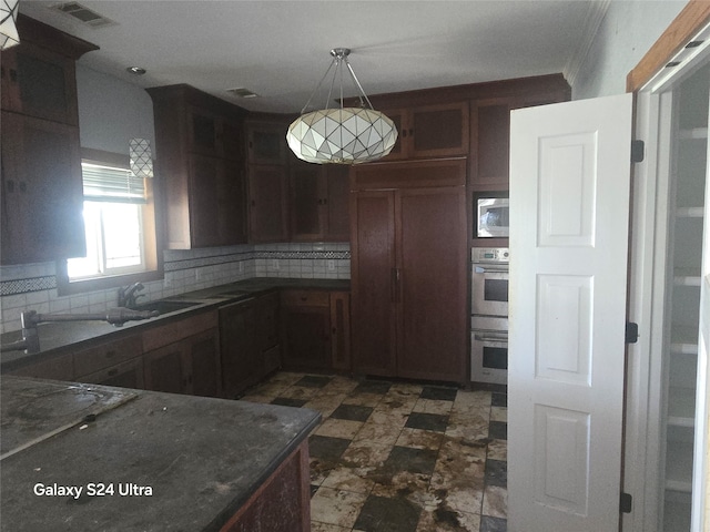 kitchen with appliances with stainless steel finishes, dark tile patterned floors, sink, backsplash, and decorative light fixtures