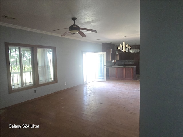 unfurnished living room featuring sink, ceiling fan with notable chandelier, crown molding, and hardwood / wood-style floors