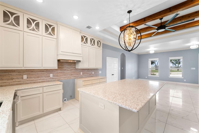 kitchen with beam ceiling, hanging light fixtures, backsplash, a tray ceiling, and a kitchen island