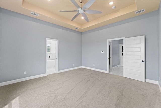 empty room with light carpet, a raised ceiling, and ceiling fan