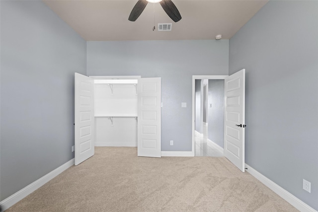 unfurnished bedroom featuring light carpet, a closet, a spacious closet, and ceiling fan